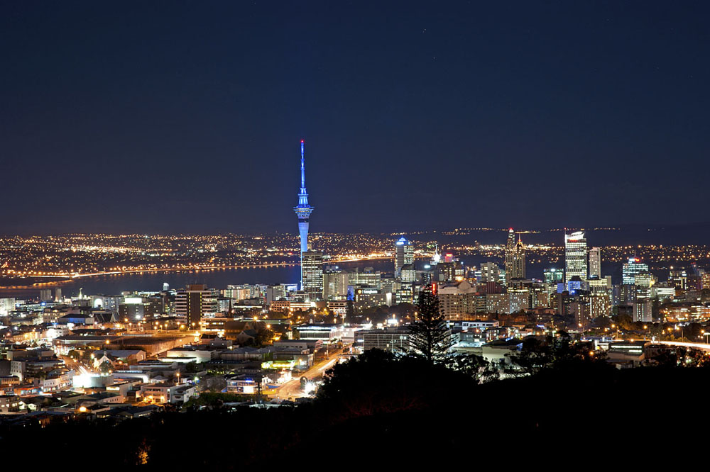A stunning panoramic view of Auckland at night showcases the illuminated skyline, with the iconic Sky Tower standing tall against a backdrop of twinkling city lights and the serene waterfront. section 2